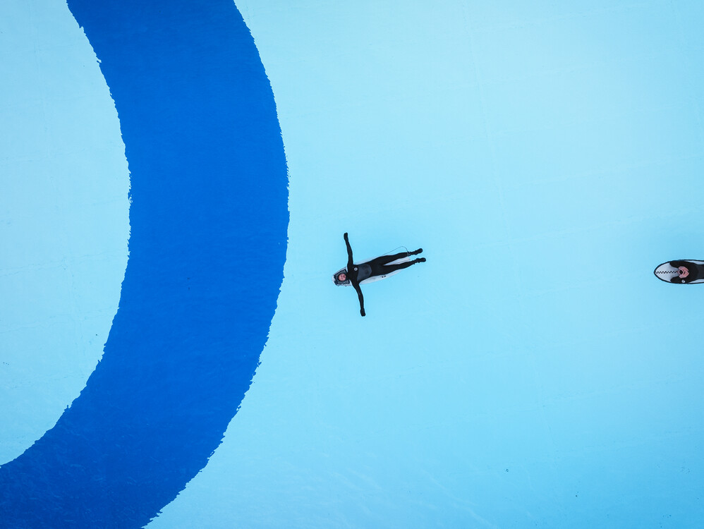 Die Surftown soll ein freizugänglicher Ort für alle sein, an dem man sich treiben lassen und sportlich austoben kann. Das Bild zeigt einen Surfer aus der senkrechten Draufsicht, der rücklings auf seinem Board liegt, die Arme seitlich von sich gestreckt und auf seinem Board im ruhigen Wasser floatet.